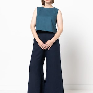 May include: A woman wearing a teal sleeveless top and wide-leg navy pants. The top has a boat neck and the pants are high-waisted. The outfit is paired with silver platform sneakers. The background is plain white.