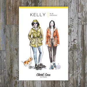 May include: A sewing pattern illustration for the Kelly Anorak, a hooded jacket with a drawstring waist. The illustration shows two women wearing the jacket in different colors, one in green and one in orange. The text "Kelly Anorak No. 09 Closet Core Patterns" is printed on the bottom of the illustration.