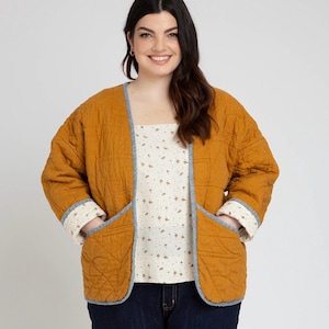 Könnte beinhalten: Eine senfgelbe gesteppte Jacke mit blauen Besätzen und Taschen. Die Jacke hat eine lockere Passform und ist vorne offen.