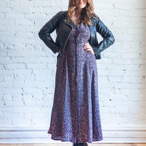 May include: A woman wearing a black leather jacket over a long floral print dress and black ankle boots.
