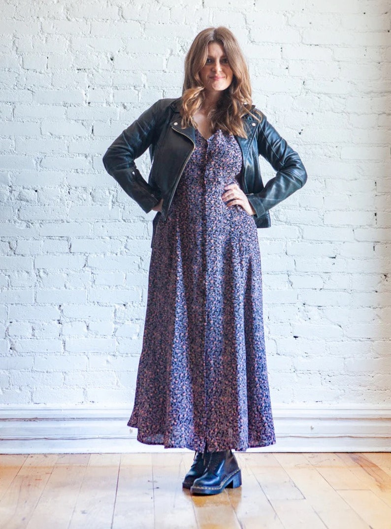 May include: A woman wearing a black leather jacket over a long floral print dress and black ankle boots.