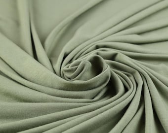 May include: Close-up of a soft, sage green fabric with a smooth texture. The fabric is draped and folded, creating a flowing, elegant look.