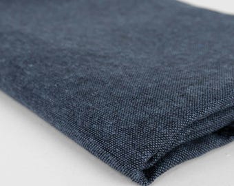 May include: Folded, dark blue fabric with a textured weave. The fabric appears to be linen or a similar material, with a slightly uneven surface. The color is a deep, muted blue, with subtle variations in tone. The fabric is folded over on itself.