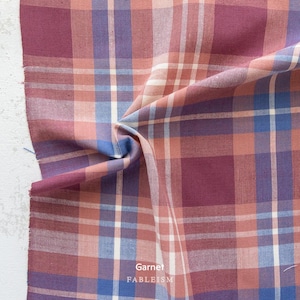 a close-up view of a fabric with a plaid pattern in shades of pink, blue, and white. The fabric appears to be folded or crumpled, creating a textured and visually interesting surface.