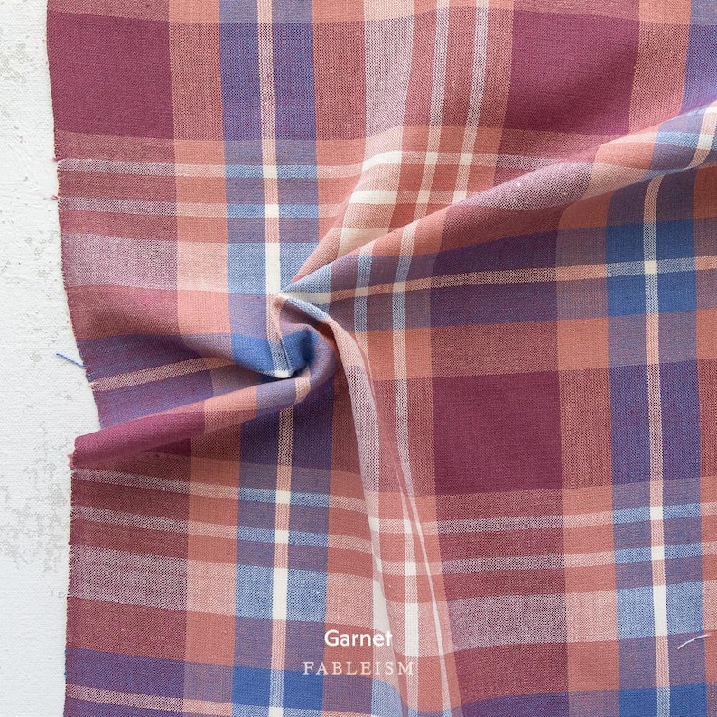 a close-up view of a fabric with a plaid pattern in shades of pink, blue, and white. The fabric appears to be folded or crumpled, creating a textured and visually interesting surface.
