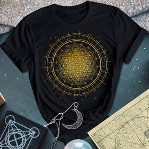 May include: Black t-shirt with a gold geometric design of a flower of life pattern. The design is surrounded by a circle with a dotted border.