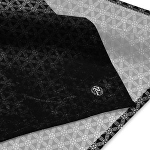 May include: Black and white fabric with a geometric pattern. The fabric is folded in half, revealing a white and gray geometric pattern on the underside. The fabric has a textured surface and a subtle sheen.