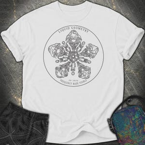 Könnte beinhalten: Ein weißes T-Shirt mit kurzen Ärmeln und einer kreisförmigen Grafik auf der Brust. Das Design zeigt ein schwarzes, komplexes, sternförmiges Muster mit dem Text "LIQUID GEOMETRY" oben und "FP 2026 FREQUENCY MADE VISIBLE" unten.