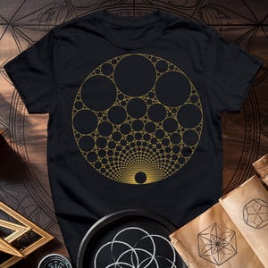 Op de afbeelding: Een zwart T-shirt met een gouden geometrisch ontwerp van een cirkel gevuld met kleinere cirkels.