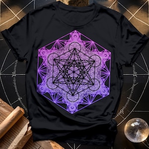 以下が含まれることがあります： 紫とピンクの幾何学模様が施された黒いTシャツ。デザインは、線と円が複雑に組み合わされたもので、神聖幾何学のマンダラに似ています。