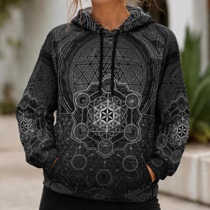 May include: A black and grey hooded sweatshirt featuring an intricate, all-over geometric pattern. The design includes complex sacred geometry motifs, such as the flower of life and star tetrahedrons, printed across the front, sleeves, and hood.