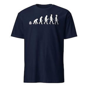 Peut inclure: T-shirt bleu marine avec un motif blanc représentant l'évolution de la vie, se terminant par une figure d'extraterrestre. Le design commence par un champignon et progresse à travers diverses étapes hominidés. Un design humoristique et stimulant.