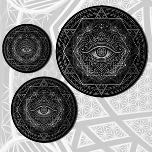 Op de afbeelding: Drie zwart-witte cirkelvormige ontwerpen met een oogsymbool in het midden, omringd door geometrische patronen. De ontwerpen zijn van verschillende groottes, met gedetailleerde, symmetrische patronen. De achtergrond heeft een herhalend geometrisch patroon.