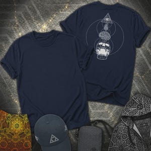May include: A dark navy blue t-shirt featuring a white line art graphic of a skull, a brain, and an eye within a triangle. The design is positioned on the back of the shirt. The front of the shirt is plain dark navy blue fabric.