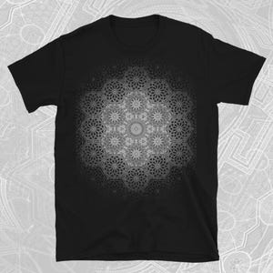 Puede incluir: Camiseta negra con un diseño de mandala simétrico y detallado en tonos grises. El intrincado patrón cubre la parte delantera de la camiseta, creando un efecto visual llamativo. El diseño está centrado y parece haber sido creado digitalmente.