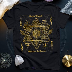 Könnte beinhalten: Schwarzes T-Shirt mit einem goldenen geometrischen Design mit Text, der "Know Thyself" und "Wisdom Is Power" lautet. Das Design enthält Symbole, einen Stern und weiteren Text. Das Shirt besteht aus einem weichen Material.