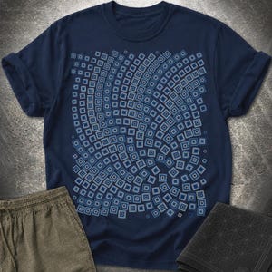 May include: A navy blue short-sleeve t-shirt featuring a central graphic print of numerous small, light blue squares arranged in a swirling, vortex-like pattern across the chest area. The shirt has a crew neckline and rolled sleeve cuffs.
