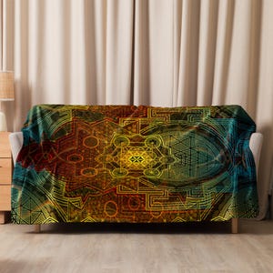 May include: A throw blanket with a geometric design in shades of yellow, orange, red, and teal. The pattern features symmetrical shapes and lines, creating a complex and visually appealing design. The blanket is draped over a sofa.