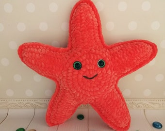 Puede incluir: Una estrella de mar de peluche de color rojo brillante con ojos verdes y una boca sonriente. La estrella de mar está hecha de un material suave y peludo y es perfecta para acurrucarse.