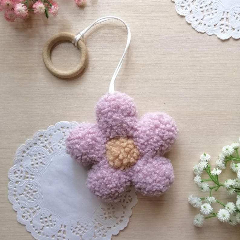 Pode incluir: Uma flor de cor roxa clara e felpuda com um centro de cor laranja claro, presa a um anel de madeira com um cord&atilde;o branco.