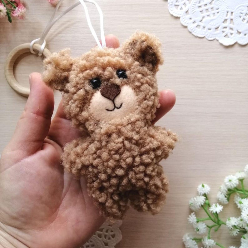 Pode incluir: Um pequeno urso de peluche castanho com textura felpuda. O urso tem olhos pretos, um nariz castanho e um sorriso costurado.