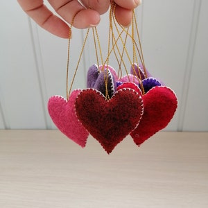 May include: Five felt heart ornaments in shades of pink, red, and purple, hanging from gold strings.