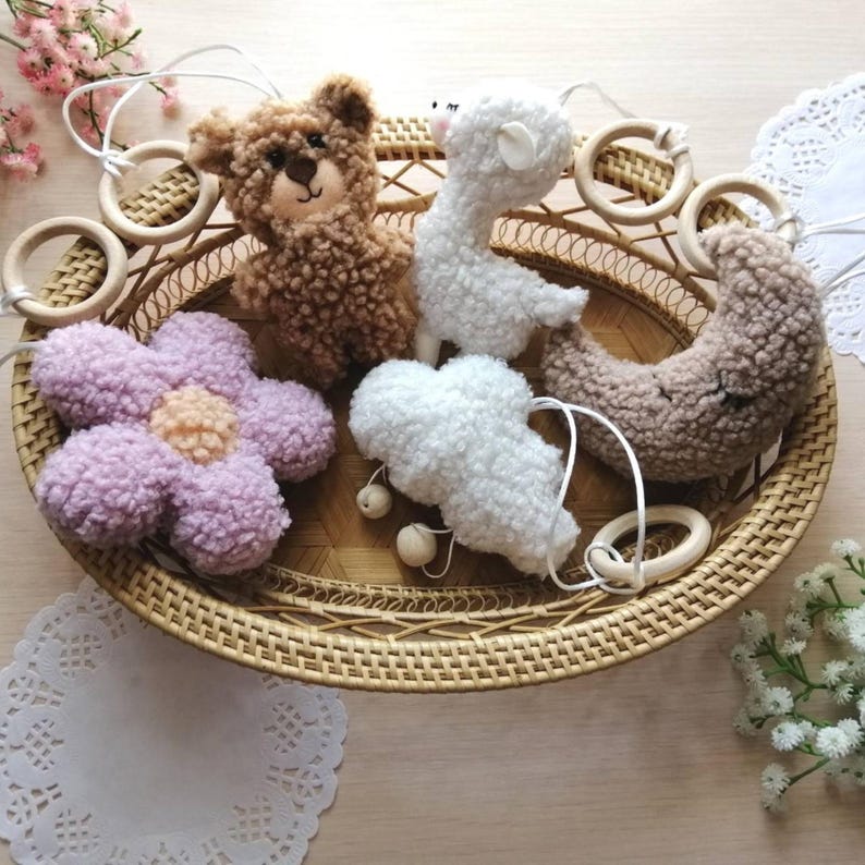 Pode incluir: Um m&oacute;bile para beb&ecirc; com um urso marrom, uma lhama branca, uma flor roxa, uma nuvem branca e uma lua crescente marrom. O m&oacute;bile &eacute; feito de tecido macio e felpudo e tem an&eacute;is de madeira.