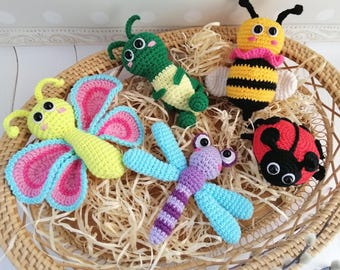May include: Five crocheted stuffed animals in a wicker basket. The animals are a butterfly with pink and blue wings, a green caterpillar, a yellow and black bee, a purple and blue dragonfly, and a red ladybug.