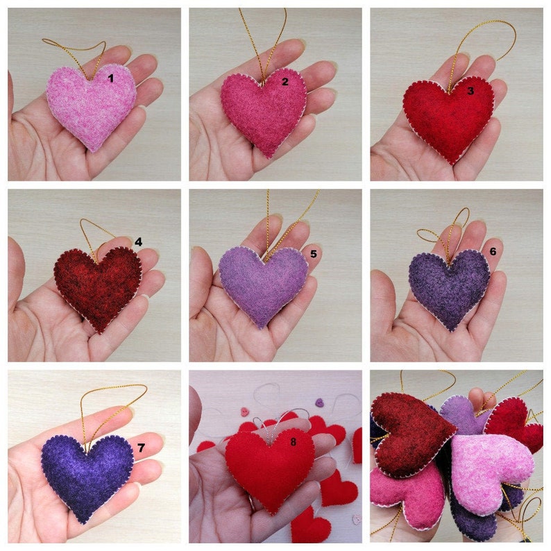 May include: Nine felt heart ornaments in various colors, including pink, red, purple, and lavender. The hearts are strung on gold cords and have white stitching around the edges.