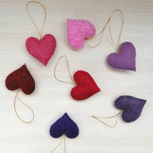 May include: Seven felt heart ornaments in various colors, including red, pink, purple, and burgundy. Each heart has a gold string attached for hanging.