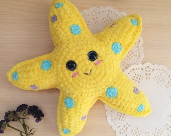 Puede incluir: Una estrella de mar de crochet amarilla con una cara sonriente y lunares azules y morados.
