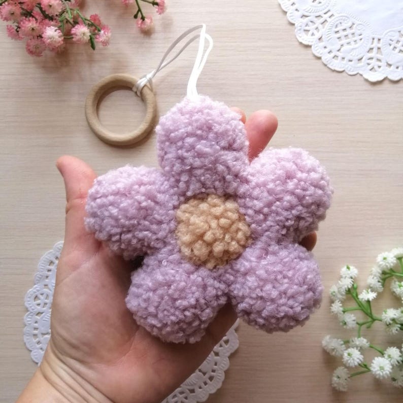 Pode incluir: Uma flor macia e felpuda de cor lavanda com um centro castanho claro. A flor est&aacute; presa a um cord&atilde;o branco e um anel de madeira.