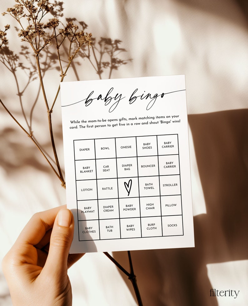 May include: A white baby bingo card with black text. The card has a grid of 25 squares with different baby-related items listed in each square. The items include diaper, bowl, onesie, baby shoes, baby carrier, baby blanket, car seat, diaper bag, bouncer, baby carrier, lotion, rattle, bath towel, stroller, baby playmat, diaper cream, baby powder, high chair, pillow, baby clothes, bath tub, baby wipes, burp cloth, and socks.