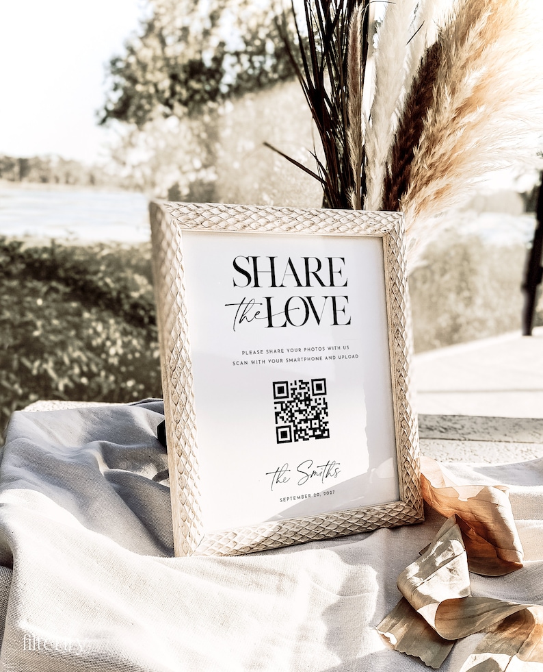 May include: A white sign with a black frame and a black and white QR code. The sign reads "Share the Love" and "Please share your photos with us. Scan with your smartphone and upload." The sign also includes the text "The Smiths" and "September 10, 2017".