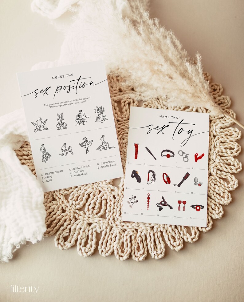 May include: Two white cards with black text and illustrations for a bachelorette party game. One card says "GUESS THE sex position" and the other says "NAME THAT sex toy". The cards are on a beige woven placemat.