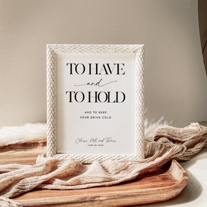 Może przedstawiać: Biały znak z czarnym tekstem, kt&oacute;ry brzmi "To Have and To Hold and to keep your drink cold." Znak zawiera r&oacute;wnież tekst "Cheers, Kate and Thomas June 10, 20XX".