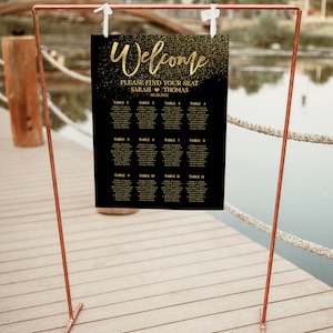May include: A black and gold wedding seating chart with the text "Welcome" and "Please find your seat" with the names Sarah and Thomas and the date 08.30.2022. The chart is on a copper stand.