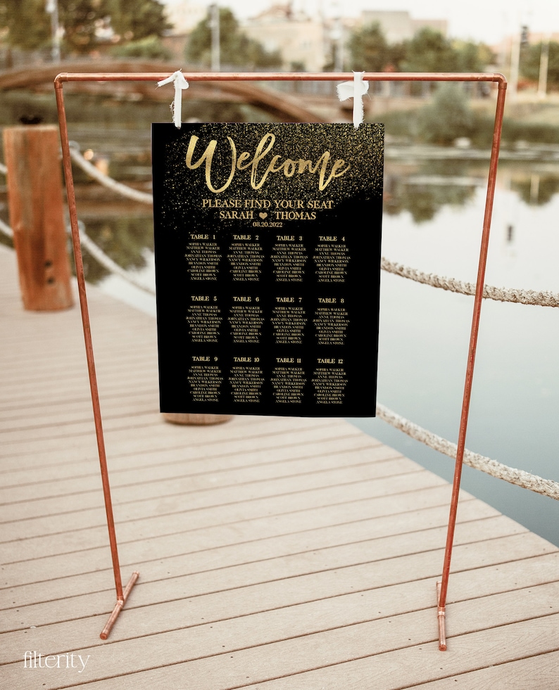 May include: A black and gold wedding seating chart with the text "Welcome" and "Please find your seat" with the names Sarah and Thomas and the date 08.30.2022. The chart is on a copper stand.