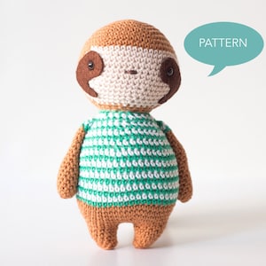 Puede incluir: Un juguete de perezoso de crochet que lleva una camisa a rayas verde y blanca. El perezoso tiene ojos marrones y una nariz marr&oacute;n. El juguete est&aacute; de pie sobre un fondo blanco. PATTERN