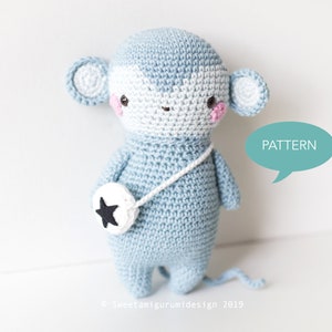 Puede incluir: Un juguete de mono de crochet azul con una estrella blanca en un círculo blanco unido a una correa blanca. El mono tiene mejillas rosadas y una cara blanca. El texto "PATTERN" está en un bocadillo de diálogo.