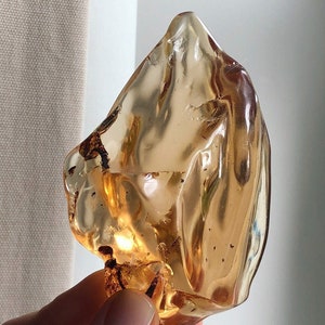 May include: A piece of amber, a translucent gemstone with a warm, golden colour. The irregular shape has a glossy surface with internal inclusions. The amber is held in a hand, highlighting its natural beauty and unique form.
