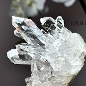 Puede incluir: Un grupo de cristales de cuarzo transparente con múltiples puntas, que muestra una estructura cristalina natural. Los cristales son transparentes, reflejan la luz y crean un efecto brillante. La imagen está sobre un fondo oscuro.