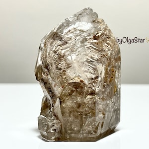 Pode incluir: Cristal de quartzo bruto e natural, de cor castanho-claro e transparente. O cristal tem uma superfície áspera e texturizada e uma forma irregular única. Espécime mineral.
