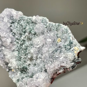 May include: A close-up of a natural mineral specimen. The crystal formation features a mix of pale lavender, clear, and dark green hues. The surface is covered in small, sparkling crystal clusters. The text "byOlgaStar" is visible.