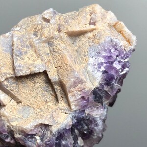 Może przedstawiać: Zbliżenie na surowy klaster kryształów ametystu. Kryształ charakteryzuje się mieszanką fioletowych i brązowych kolorów, z szorstką, teksturowaną powierzchnią. Ametyst ma warstwowy wygląd z widocznymi strukturami krystalicznymi.