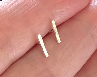May include: A pair of silver hammered bar stud earrings. The earrings are small and simple, making them a great everyday accessory.