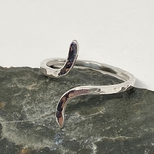 May include: A silver hammered ring with a unique, curved design. The ring is open and adjustable to fit most finger sizes.