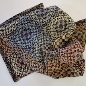 May include: A woven textile featuring a repeating geometric pattern of squares and circles in a gradient of colors including light blue, soft pink, golden yellow, and deep purple, with a dark brown border along the edges of the fabric.