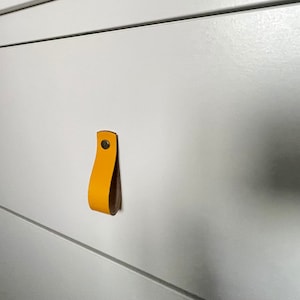 May include: A white drawer with a yellow leather pull handle.