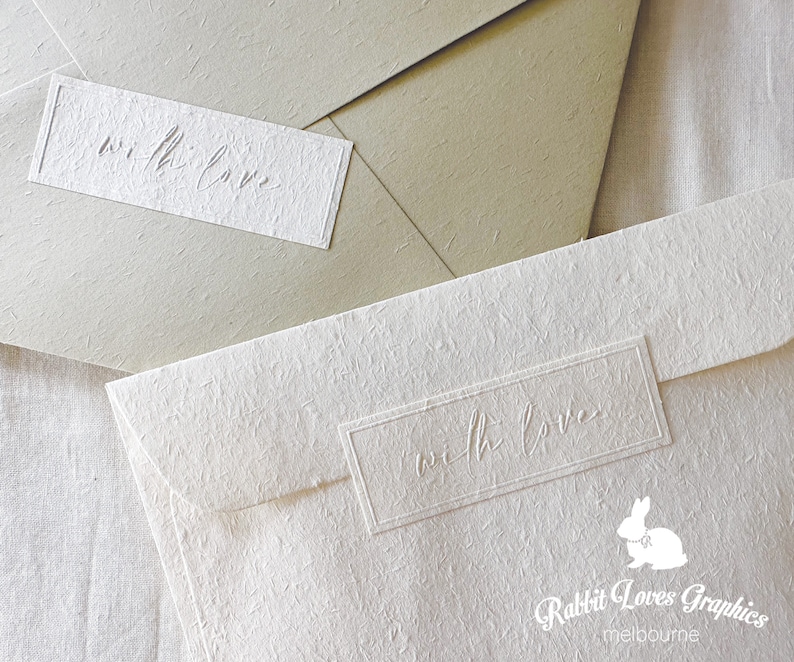 May include: Two white envelopes with a textured surface. The envelopes have a rectangular label with the text "with love" embossed on them. The bottom envelope also has the text "Rabbit Loves Graphics melbourne" printed on it.